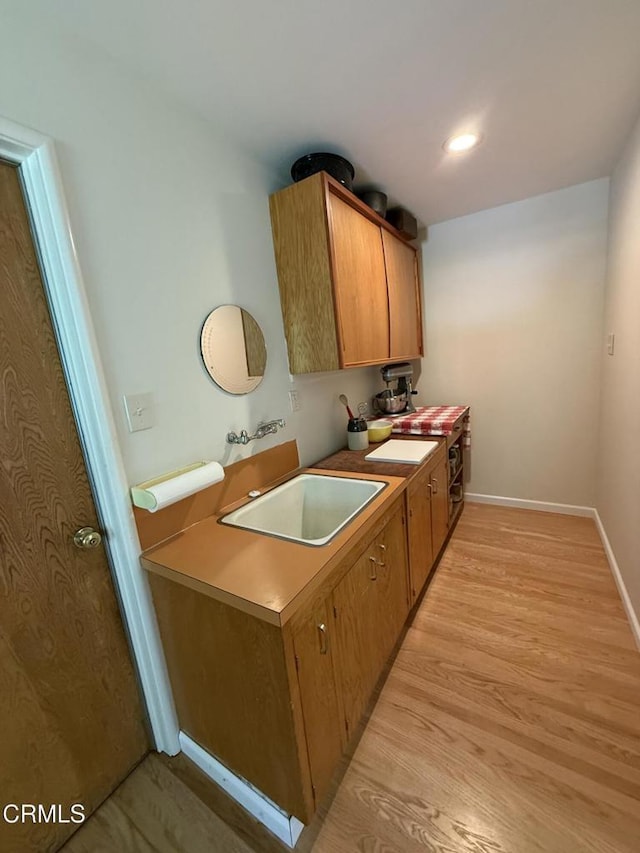 kitchen with a sink, brown cabinets, light wood finished floors, baseboards, and recessed lighting