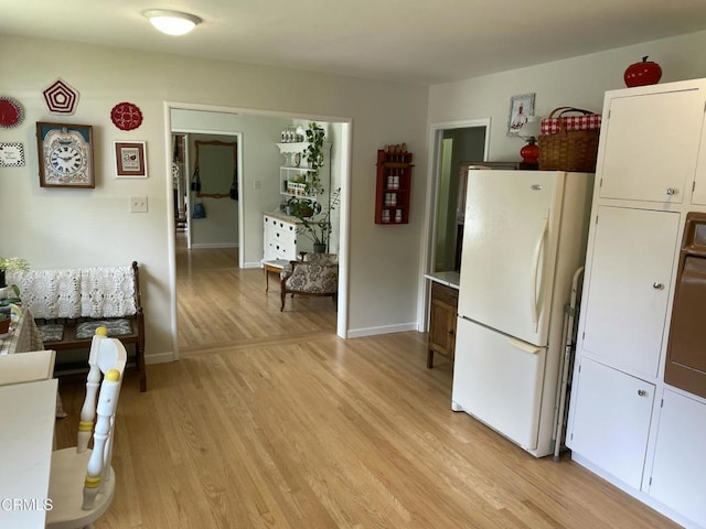 kitchen featuring light wood finished floors, baseboards, freestanding refrigerator, and white cabinetry