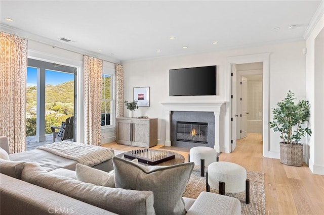 living room with recessed lighting, light wood-type flooring, ornamental molding, visible vents, and a glass covered fireplace