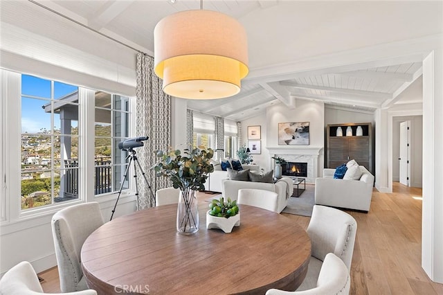 dining space featuring a high end fireplace, light wood-style flooring, and vaulted ceiling with beams