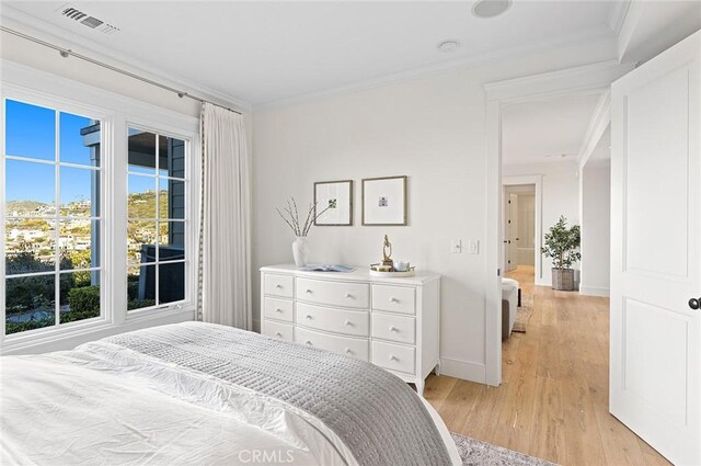 bedroom featuring baseboards, visible vents, light wood-style flooring, and ornamental molding