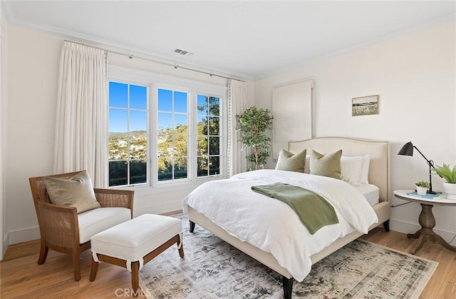 bedroom with crown molding, baseboards, light wood finished floors, and visible vents