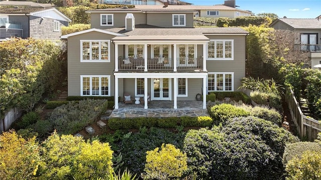rear view of property featuring a balcony, fence, a patio, a shingled roof, and french doors