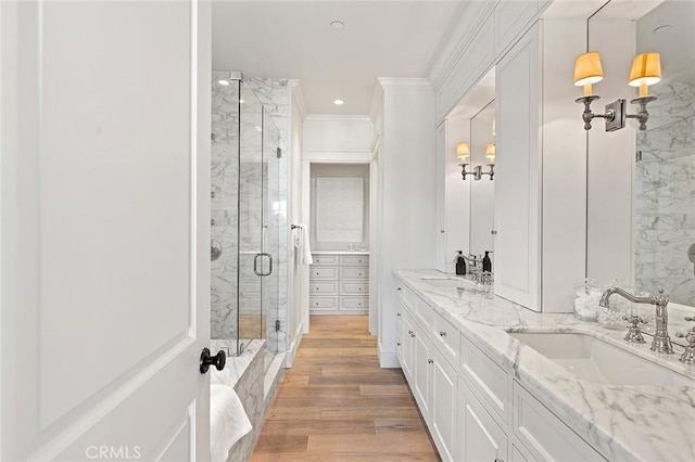 bathroom with a shower stall, crown molding, double vanity, wood finished floors, and a sink