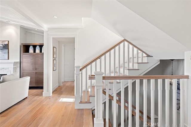 stairs featuring wood finished floors, a high end fireplace, and recessed lighting