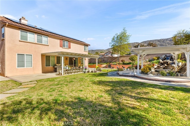 back of house with stucco siding, a pergola, roof mounted solar panels, a patio, and a lawn
