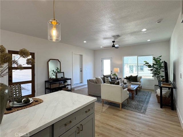 living room with light wood-type flooring, a ceiling fan, a textured ceiling, and recessed lighting