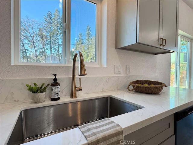 details with a textured wall, light stone counters, a sink, dishwasher, and gray cabinetry