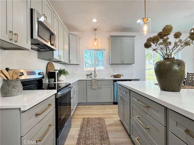 kitchen featuring appliances with stainless steel finishes, a sink, light wood-style flooring, decorative light fixtures, and gray cabinetry