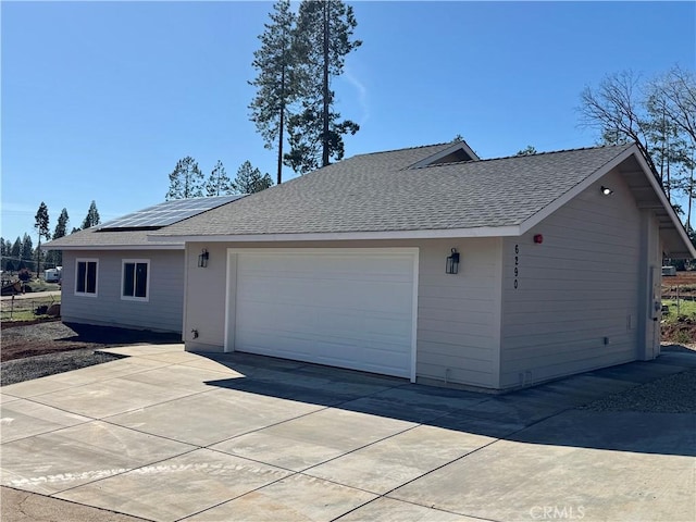 view of side of home with roof mounted solar panels, roof with shingles, and concrete driveway
