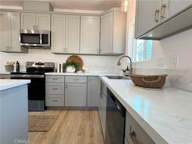 kitchen featuring a sink, appliances with stainless steel finishes, gray cabinets, and light stone counters