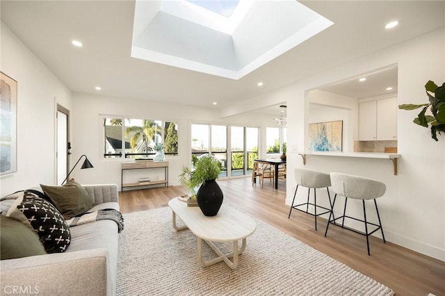 living room featuring a tray ceiling, a skylight, recessed lighting, and light wood-style floors