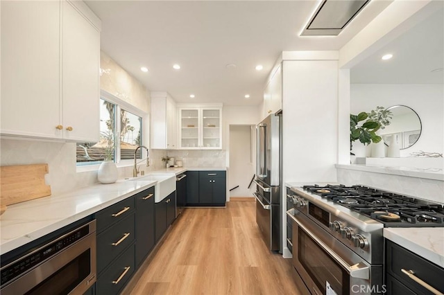 kitchen with tasteful backsplash, white cabinets, a sink, stainless steel appliances, and light wood-style flooring