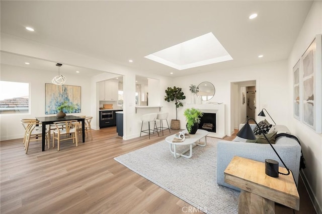 living area with a fireplace, recessed lighting, light wood-style floors, and a skylight