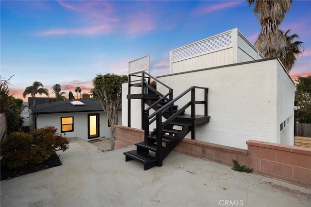 back of property at dusk with a patio area, stucco siding, and fence
