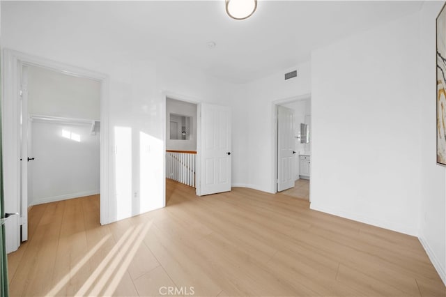unfurnished bedroom featuring a spacious closet, baseboards, light wood finished floors, and visible vents