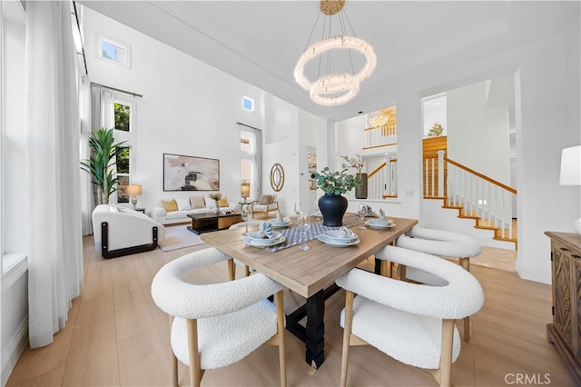 dining area featuring light wood-style flooring, stairs, a towering ceiling, and a notable chandelier