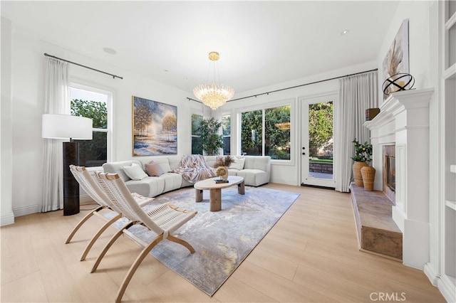 living room with a glass covered fireplace, light wood-type flooring, and a notable chandelier