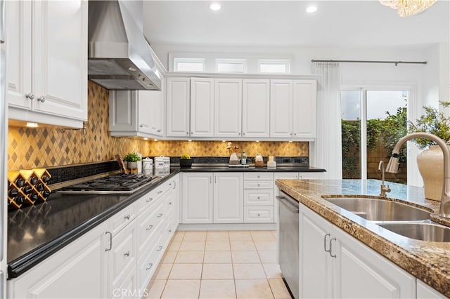 kitchen featuring wall chimney range hood, light tile patterned floors, a sink, appliances with stainless steel finishes, and backsplash