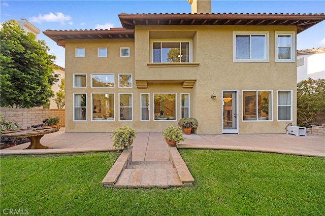 rear view of house with a patio, a lawn, and stucco siding