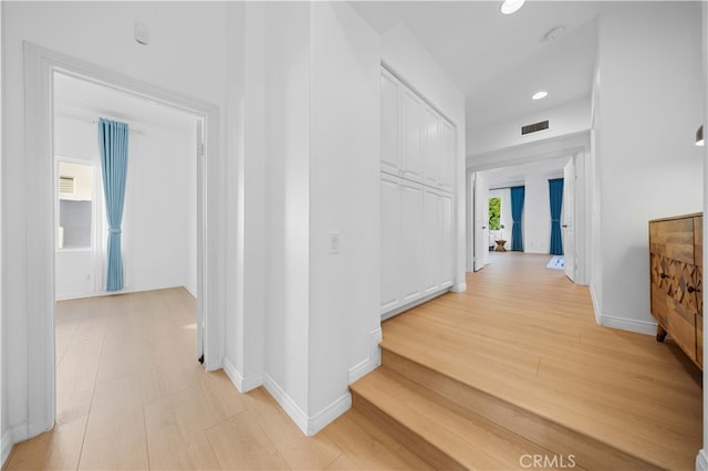 hall featuring visible vents, baseboards, and light wood-type flooring