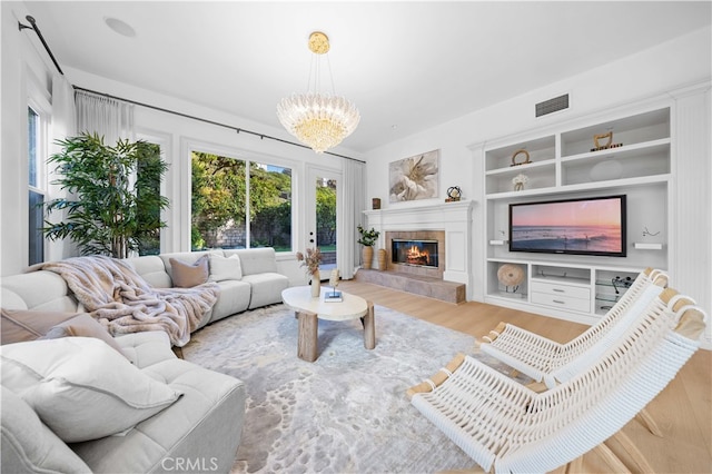 living room featuring visible vents, an inviting chandelier, built in features, wood finished floors, and a tile fireplace