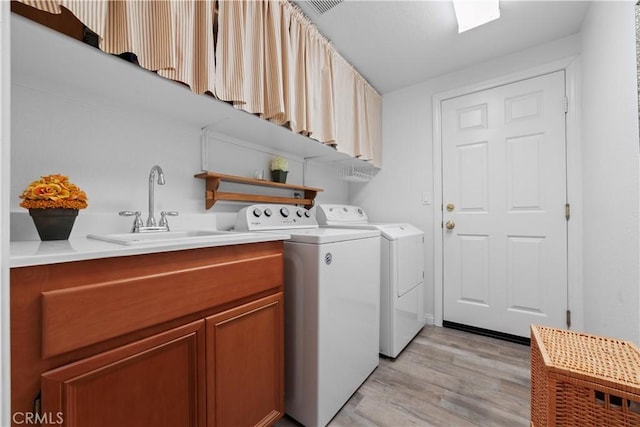 clothes washing area featuring independent washer and dryer, light wood-style floors, cabinet space, and a sink