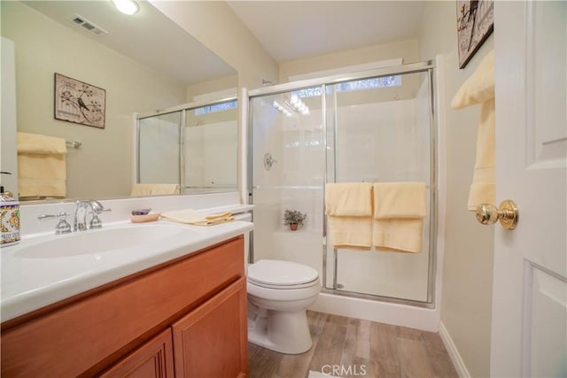 bathroom with toilet, vanity, a shower stall, wood finished floors, and visible vents