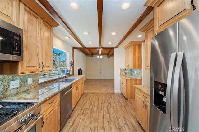 kitchen featuring light stone counters, a sink, tasteful backsplash, light wood-style flooring, and stainless steel appliances