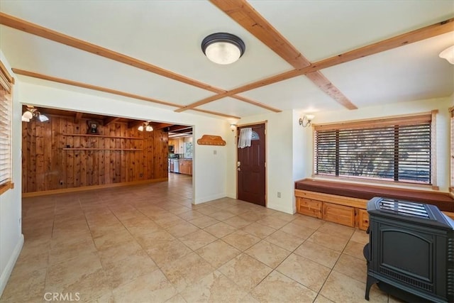 kitchen with baseboards, wooden walls, beamed ceiling, and a wood stove