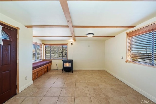 foyer with baseboards, a wood stove, and beam ceiling