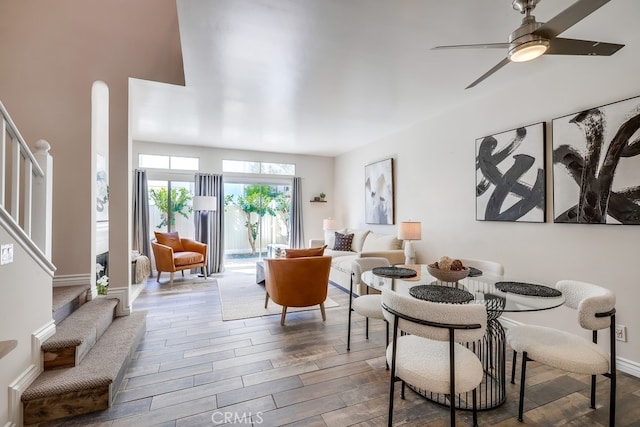 dining space featuring baseboards, ceiling fan, stairs, and wood finished floors