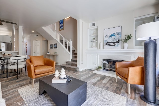 living area with visible vents, stairs, a glass covered fireplace, wood finished floors, and built in features
