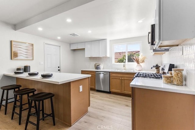 kitchen featuring visible vents, a kitchen bar, tasteful backsplash, appliances with stainless steel finishes, and light wood-style floors
