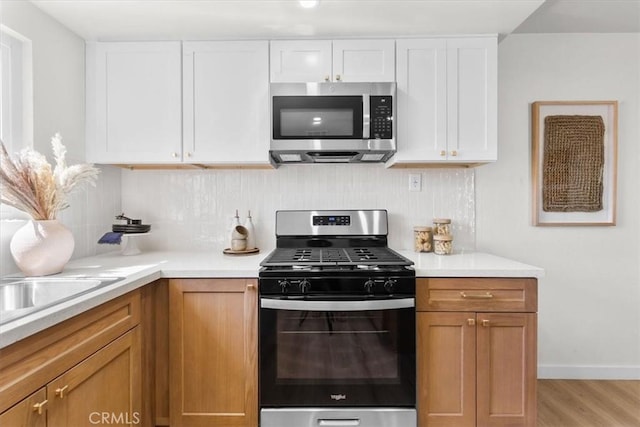 kitchen featuring decorative backsplash, light countertops, light wood-style flooring, white cabinets, and stainless steel appliances