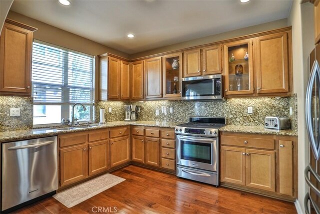 kitchen featuring tasteful backsplash, stainless steel appliances, a sink, dark wood-style floors, and light stone countertops