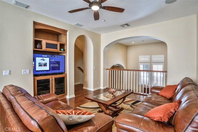 living room with visible vents, baseboards, ceiling fan, wood finished floors, and arched walkways