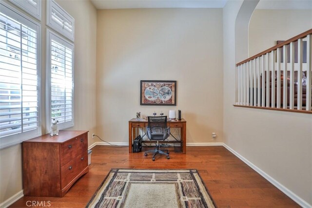 office area with baseboards, arched walkways, and wood finished floors