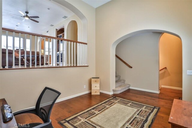 office space with arched walkways, baseboards, wood finished floors, and a ceiling fan