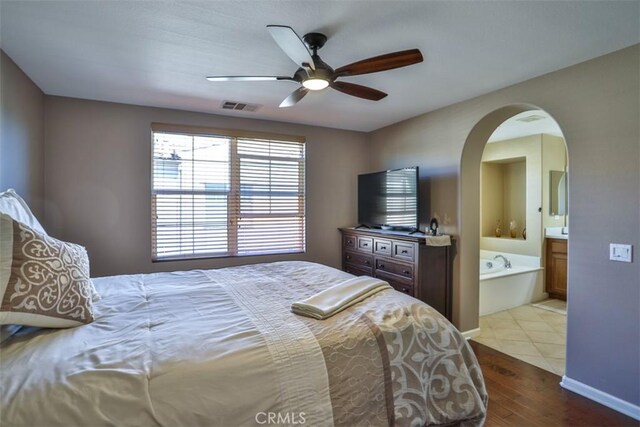 bedroom with baseboards, ensuite bath, ceiling fan, visible vents, and wood finished floors