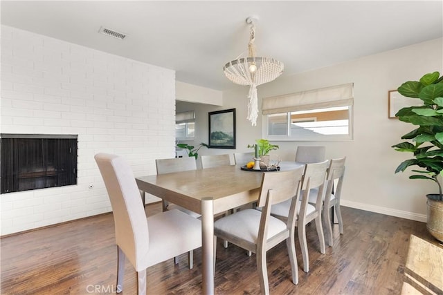 dining room featuring a fireplace, visible vents, wood finished floors, baseboards, and a notable chandelier