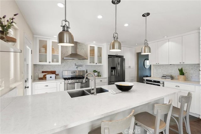 kitchen featuring glass insert cabinets, a sink, wall chimney range hood, appliances with stainless steel finishes, and backsplash