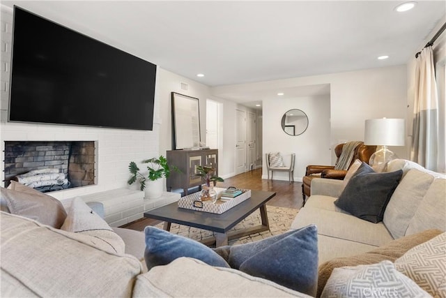 living area with wood finished floors, baseboards, a brick fireplace, and recessed lighting