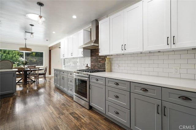 kitchen with stainless steel range with gas cooktop, wall chimney range hood, gray cabinets, light countertops, and dark wood-type flooring
