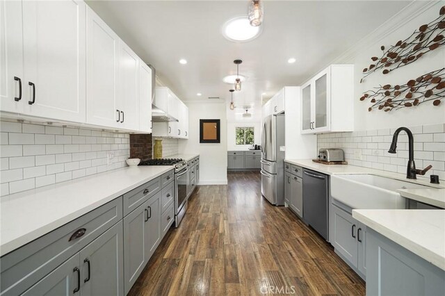 kitchen featuring a sink, gray cabinetry, glass insert cabinets, appliances with stainless steel finishes, and dark wood-style flooring