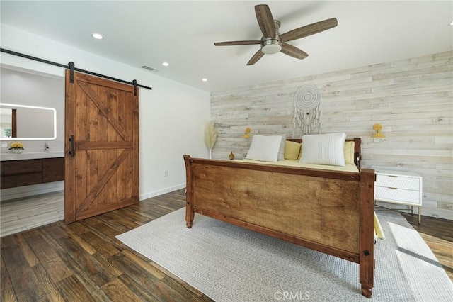 bedroom featuring a barn door, wood finished floors, wood walls, visible vents, and recessed lighting