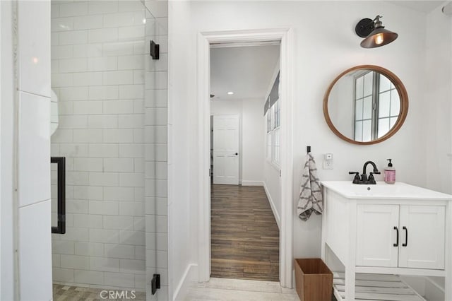 bathroom featuring baseboards, wood finished floors, vanity, and tiled shower