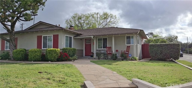 view of front facade with stucco siding, a front yard, covered porch, and a chimney