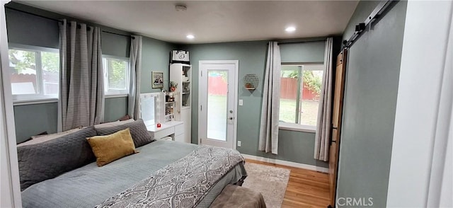 bedroom with a barn door, light wood-type flooring, recessed lighting, access to exterior, and baseboards