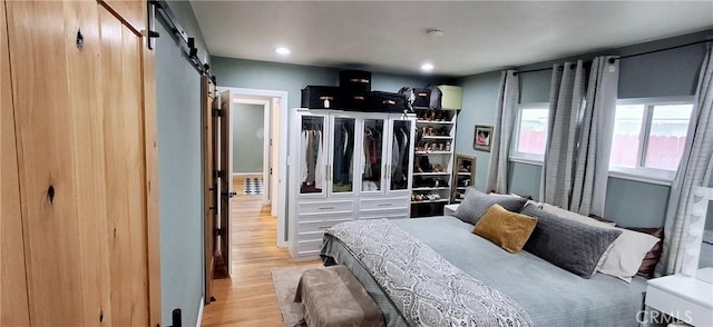 bedroom with a barn door, wood finished floors, and recessed lighting